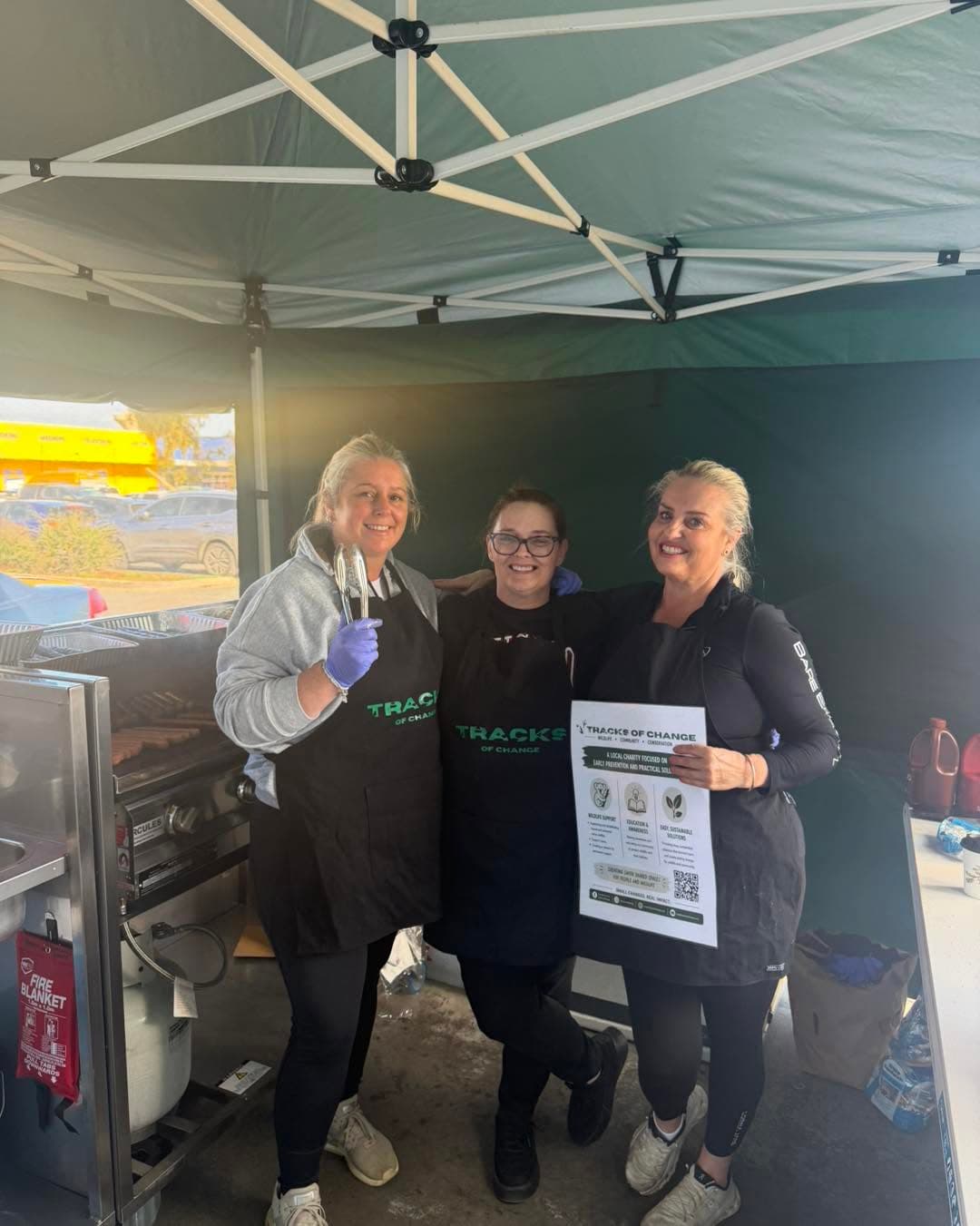 Three Tracks of Change volunteers in branded aprons at the Bunnings sausage sizzle marquee